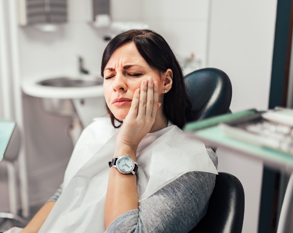 Woman holding cheek in pain before emergency dentistry