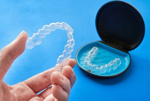 Patient holding top Invisalign aligner next to storage case