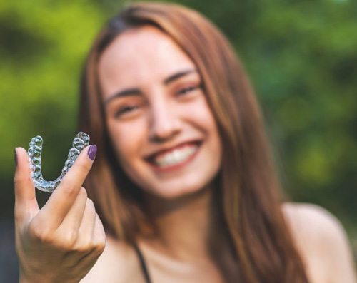 a woman smiling and holding an Invisalign aligner 