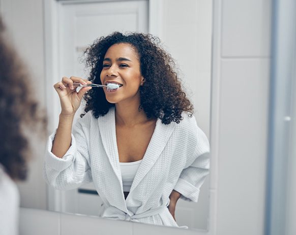Woman in front of bathroom mirror, brushing teeth