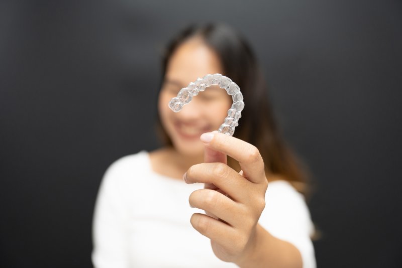 A woman smiling as she holds up her found Invisalign aligner